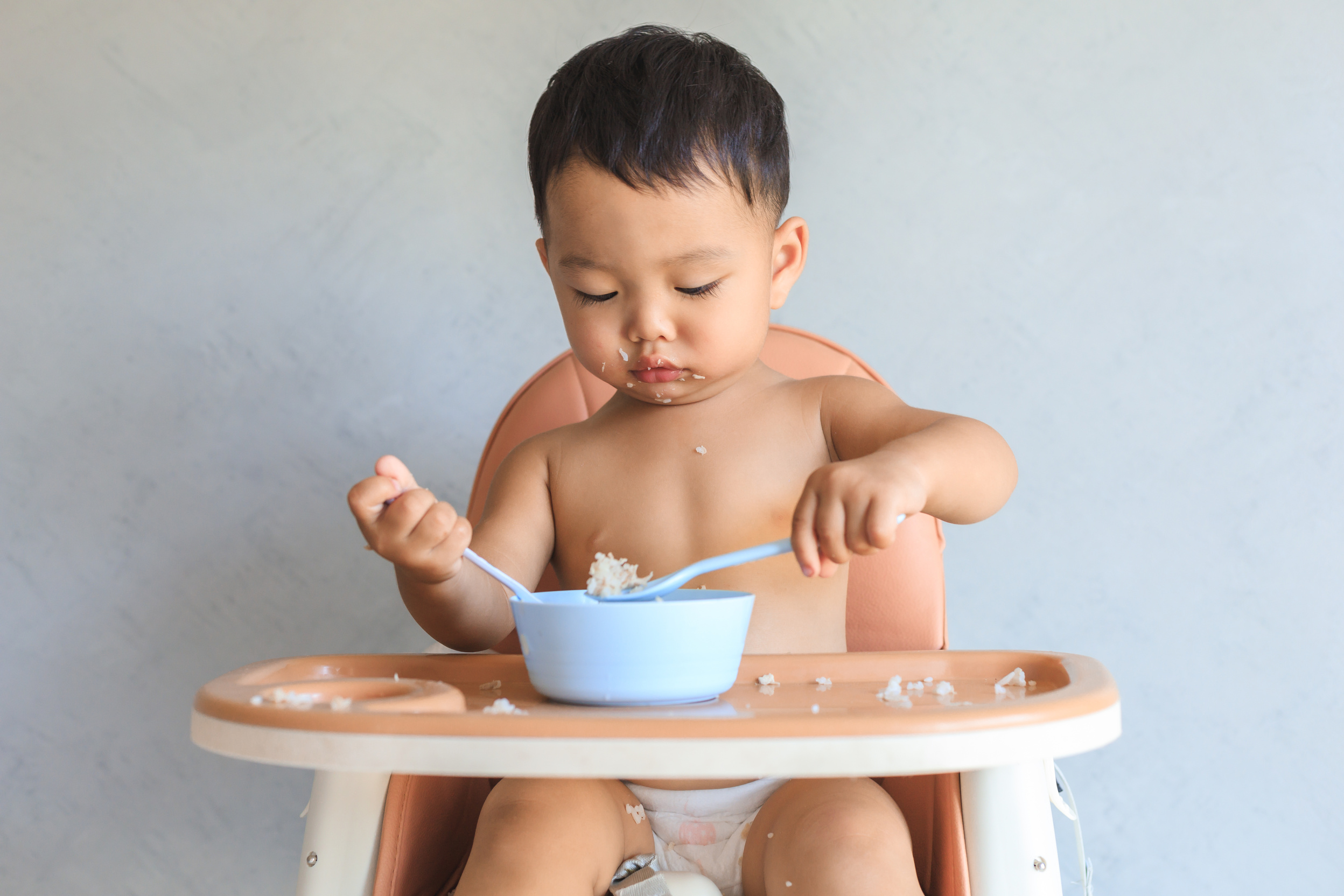 Asian baby boy eating food by himself